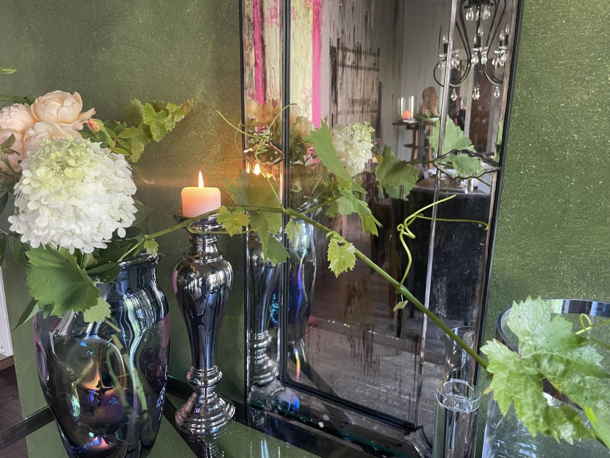Fotos aus dem Frühstücksraum Blumenarrangement mit Kerze und Spiegel vor grüner Wand.
