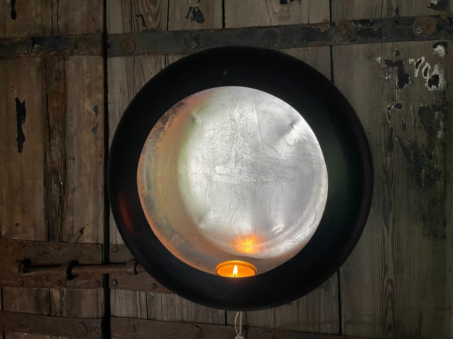 Gemütliche Stimmung Runder Metallbehälter mit einem schwachen Lichtschein im Inneren, vor einer Holzwand.