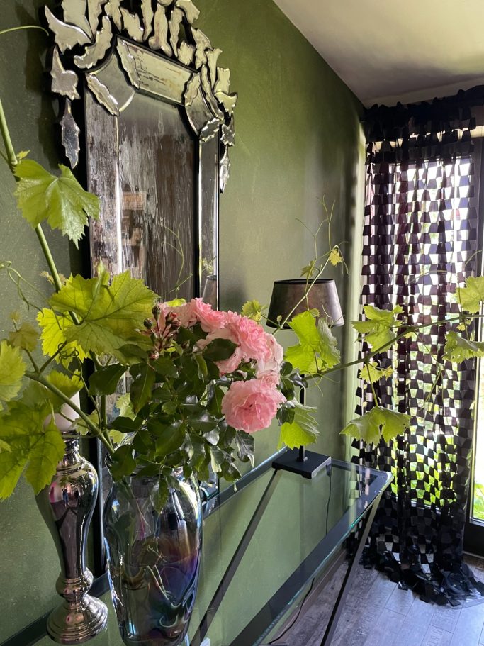Im Frühstücksraum / Detail Blumenvase mit rosa Rosen, Spiegel und schwarzes Sichtschutzgitter an der Wand.