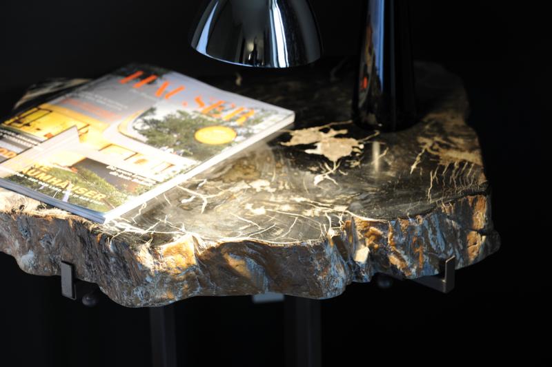 Unikate aus versteinertem Holz Holztisch mit einem Magazin und einer Lampe auf schwarzem Hintergrund.